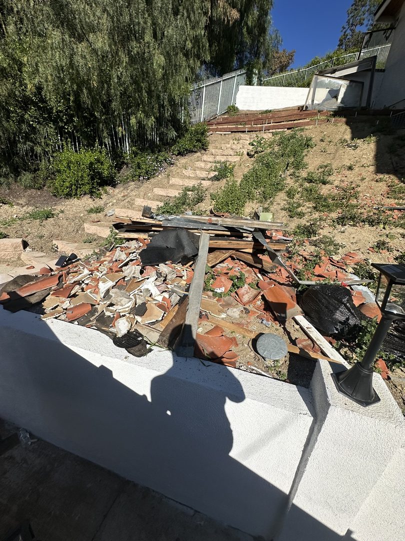 Broken roof tiles and lumber piled for junk removal on a hillside yard in Los Alamitos, California